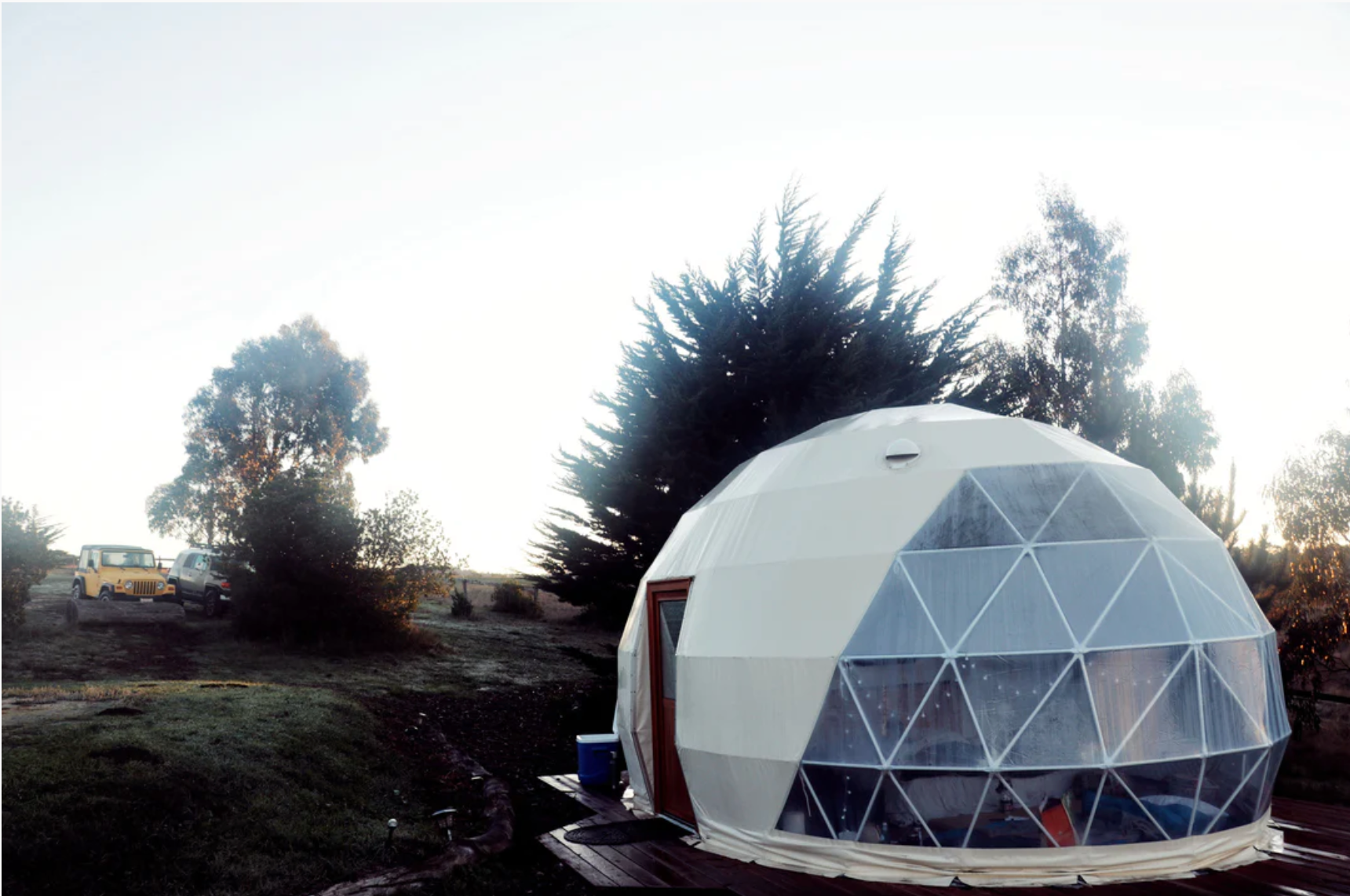 Alt text: "Geodesic dome with porthole windows set in a scenic outdoor location, ideal for glamping or use as a backyard office. This large dome tent offers a stylish and sustainable living solution, perfect for those interested in luxury Airbnb experiences or creating a unique art studio space."