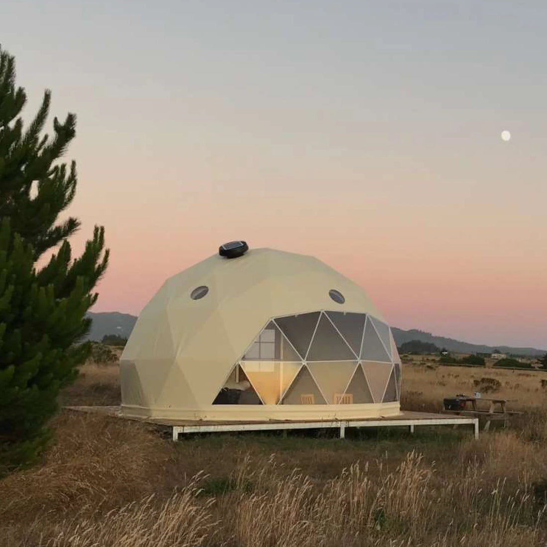Alt text: "Geodesic dome house with porthole windows set in a scenic outdoor location at sunset, showcasing a stylish and sustainable glamping solution. Ideal for luxury Airbnb, backyard dome, or art studio use."
